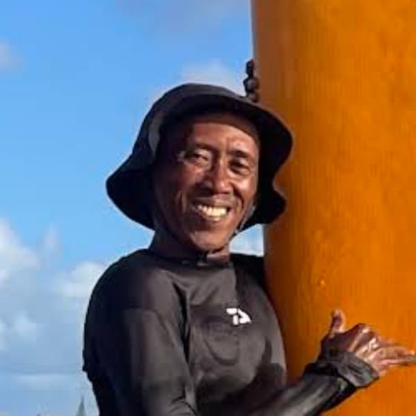 Harry Surf instructor smiling beside a surfboard on Kuta Beach